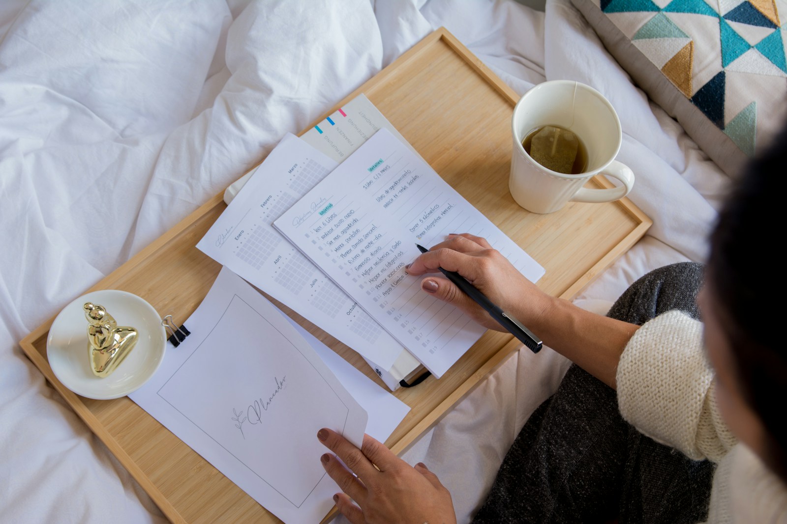 person holding white printer paper near white ceramic mug on white textile